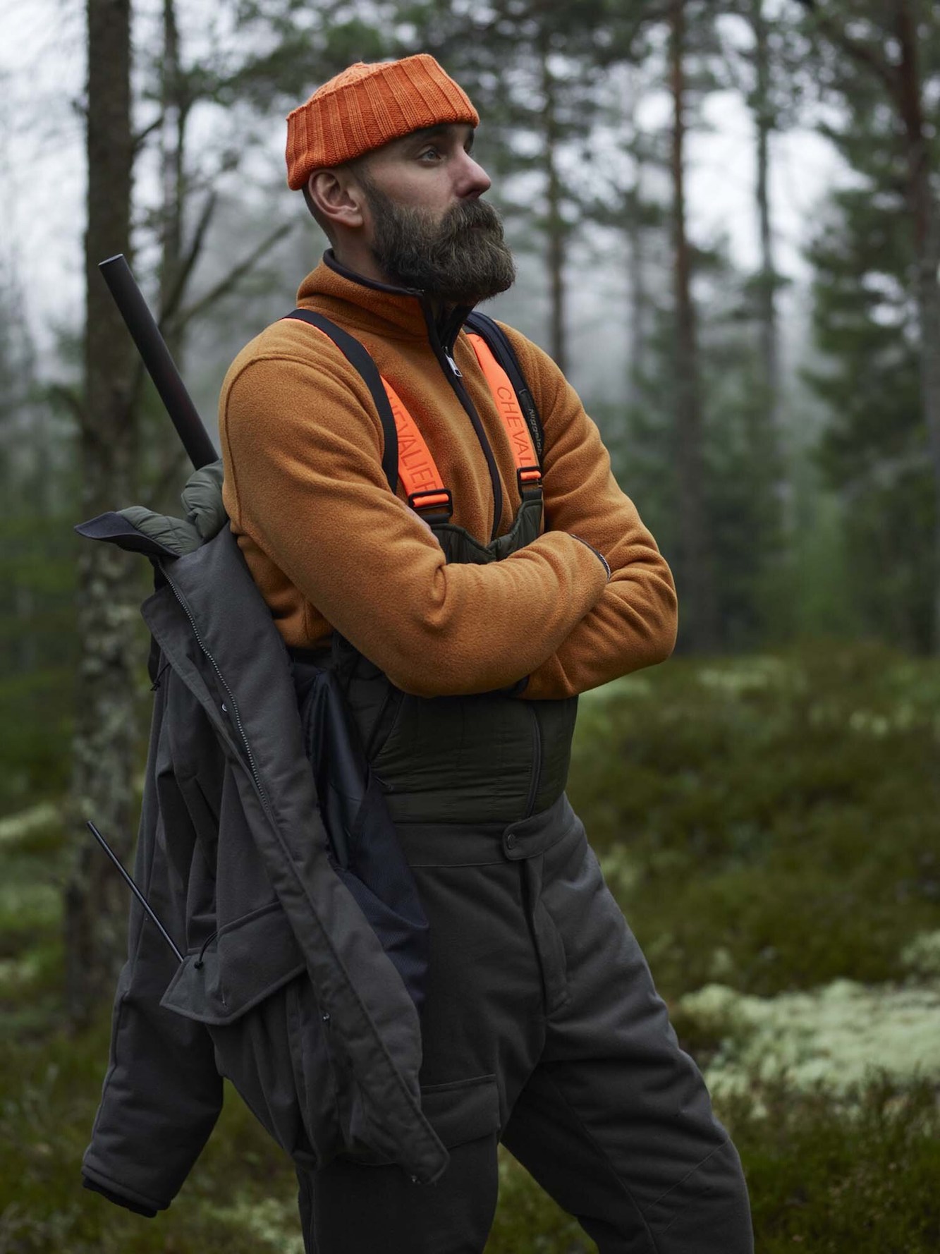 chevalier-herren-winterjacke-frost.... Die Chevalier Herren Winterjacke Frost in der Farbe Grün besteht aus warmer Wattierung und wasserfester Membran. Sie verfügt über eine verstellbare Kapuze, verstellbaren Taillenbund, zahlreiche Taschen und Codura Verstärkung an der Schulter. Auf dem Bild ist ein Jäger im Wald mit an Schulterriemen hängender Jacke.