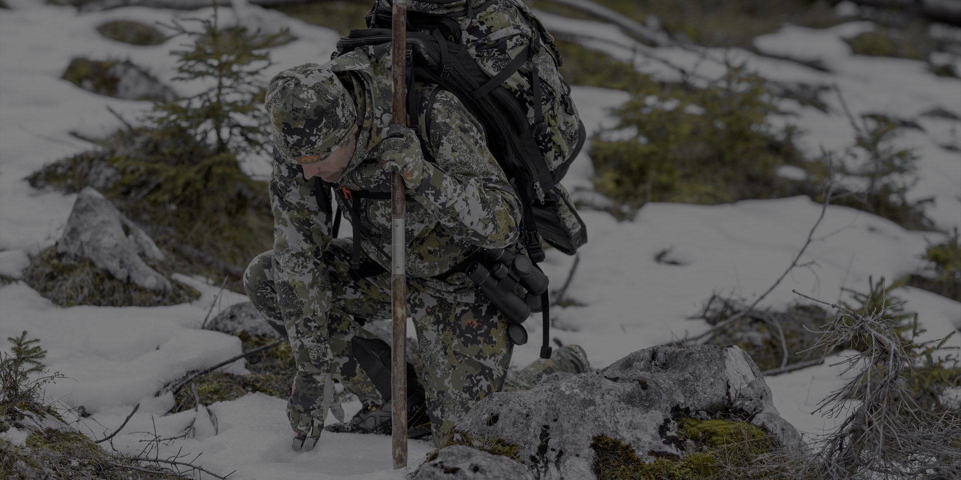 Die Blaser Herren Jacke Huntec Resist 3L in Camo-Tarrnmuster verfügt über ein 3 lagiges Gewebe und 2 Einschubtaschen sowie 2 Brusttaschen. Die Kapuze ist verstellbare. Auf dem Bild besteigt ein Herr mit Rucksack den Berg.